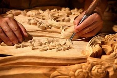 Seorang pengrajin Jepara tengah fokus membuat ukiran kayu dengan pola yang rumit, menunjukkan seni tradisional khas yang penuh presisi dan detail.